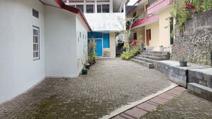 A narrow cobblestone alleyway between buildings with a blue door and a staircase leading to a balcony. - Hotel STIPRAM Kaliurang Yogyakarta (Pakem)