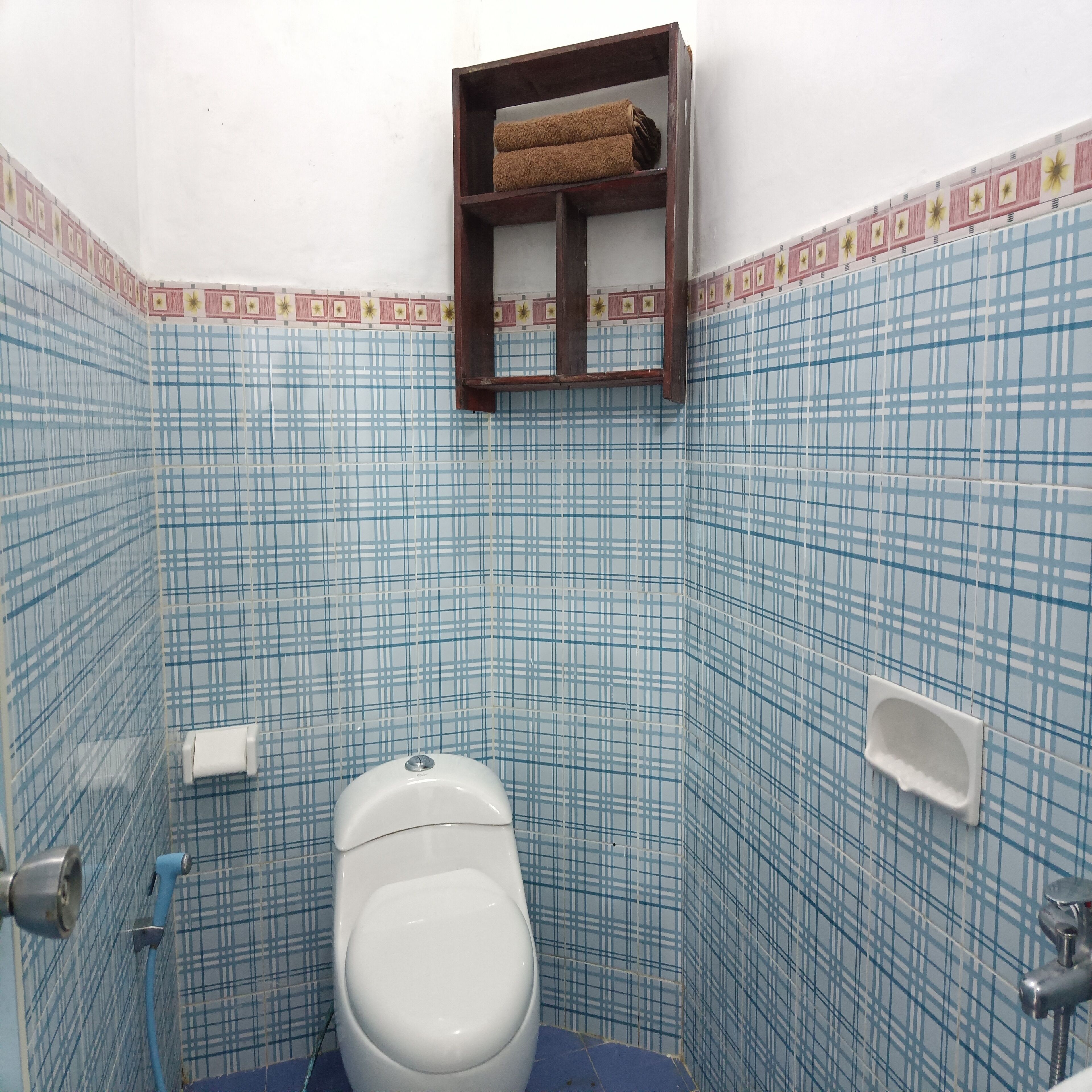 Egy kis fürdőszoba, amelyben WC, törölközőtartó és zuhanyzó található.