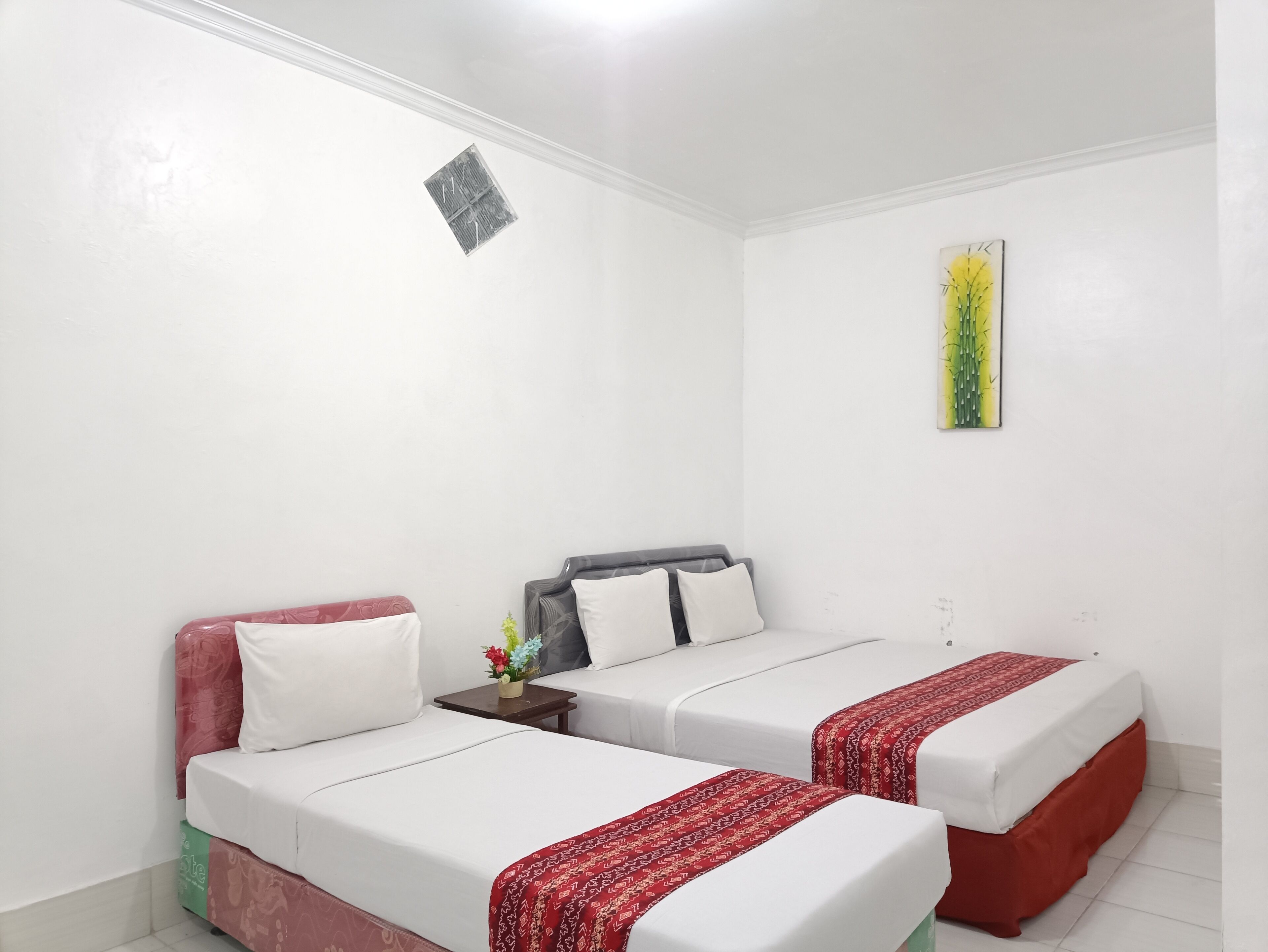 Une chambre d’hôtel avec deux lits, une petite table surmontée d’un vase de fleurs et une œuvre d’art accrochée au mur.