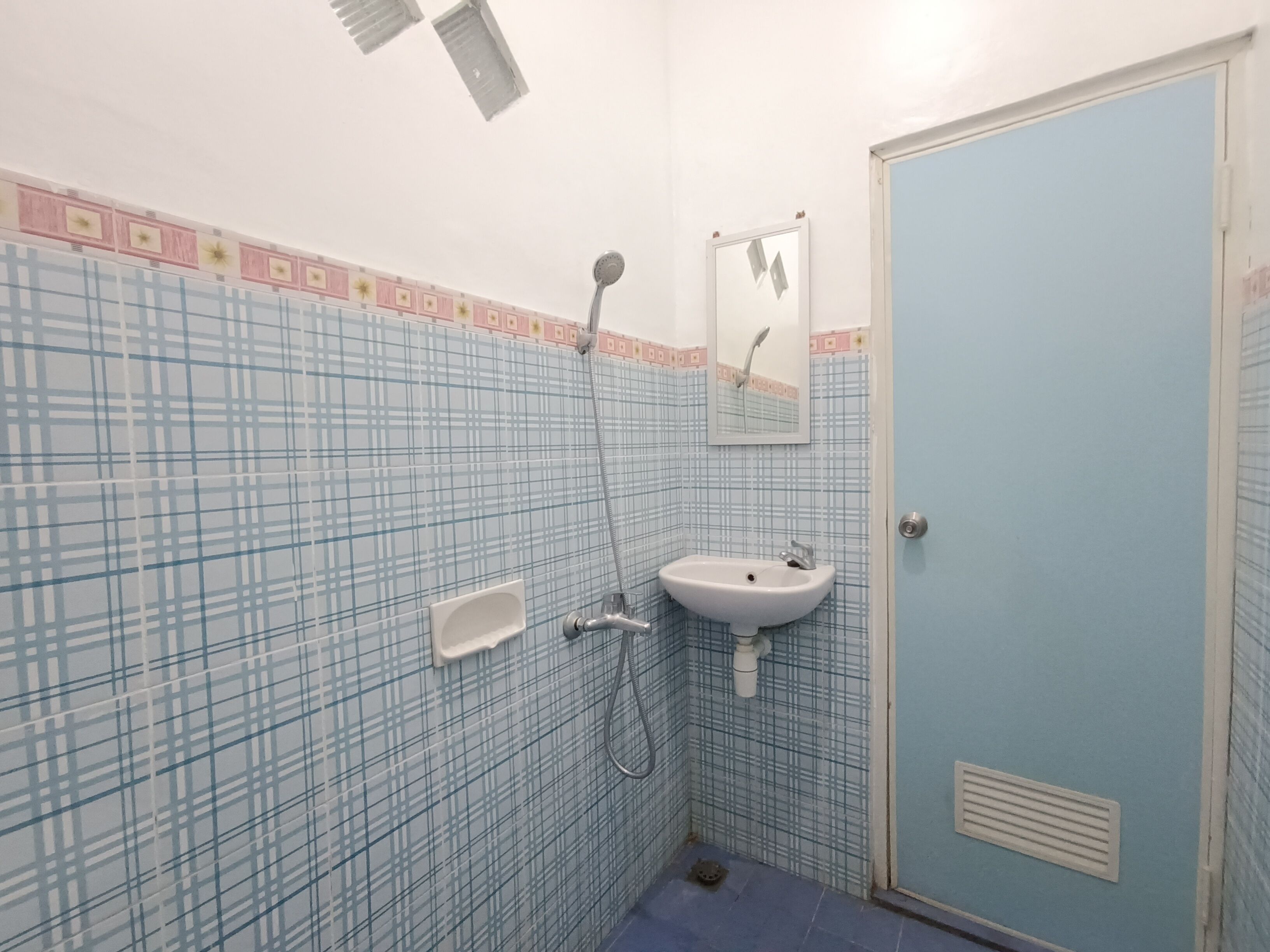 A bathroom with a blue tiled wall, a white sink, a shower, and a door.