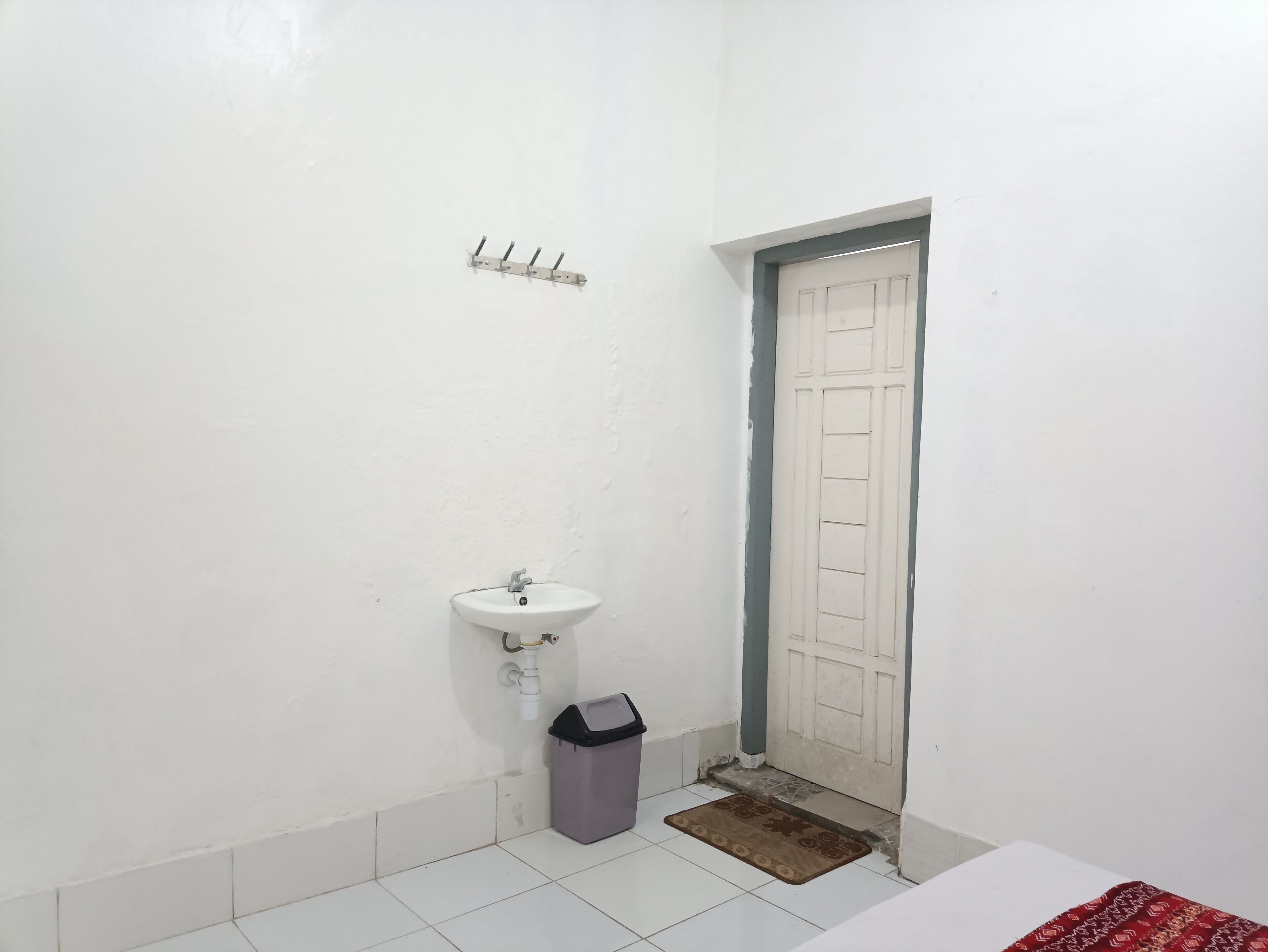 A small bathroom with a white sink, a trash bin, and a door.