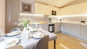 A modern kitchen with white cabinets, a dining area set for four, and a small oven. - The Tower Bridge Stateroom — 4‑Bed Penthouse w/ AC (London)