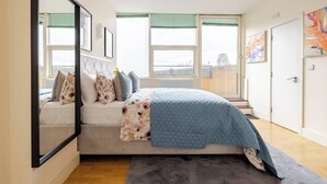 A bedroom with a bed, a large mirror, and a window with blinds. - The Tower Bridge Stateroom — 4‑Bed Penthouse w/ AC (London)