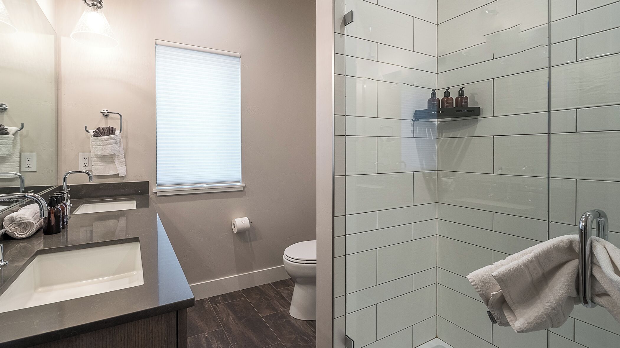 A modern bathroom with a dark countertop sink, a mirror, a toilet, and a shower area with a glass door.