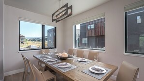A dining area with a wooden table set for six, large windows, and a view of a modern building and landscape.
