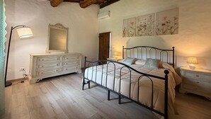 A bedroom with a bed, dresser, and two bedside tables, featuring a wooden ceiling and floral wall art.