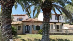 A stone house with a tiled roof, surrounded by palm trees and a white fence.