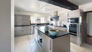 A modern kitchen with stainless steel appliances, a central island, and a black ceiling beam.