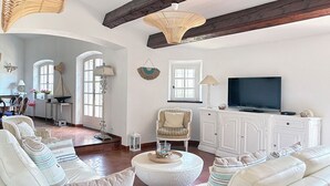 A spacious living room with white furniture, a television, and a large window.
