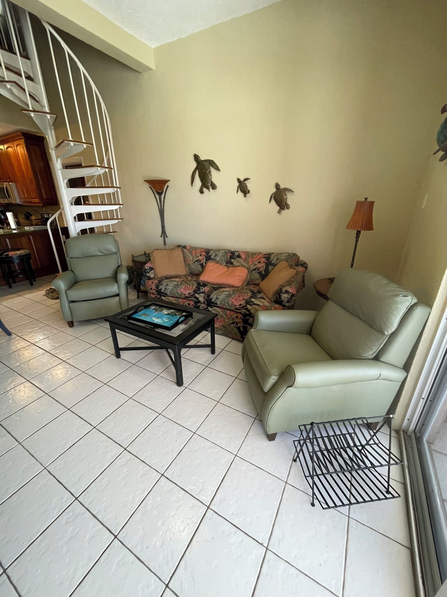 A living room with a sofa, armchairs, a coffee table, and a spiral staircase.