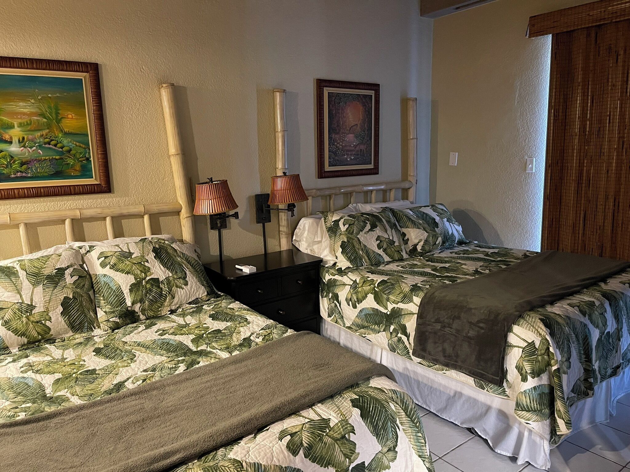 Une chambre avec deux lits, chacun recouvert d’une couvre-lit orné de motifs tropicaux, une table de chevet avec des lampes et un tableau encadré accroché au mur.