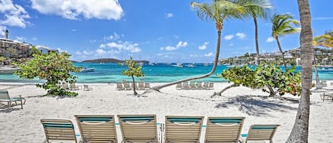 A beach with white sand, several lounge chairs, and palm trees.