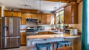 A kitchen with wooden cabinets, stainless steel appliances, a large island with stools, and a window with curtains.