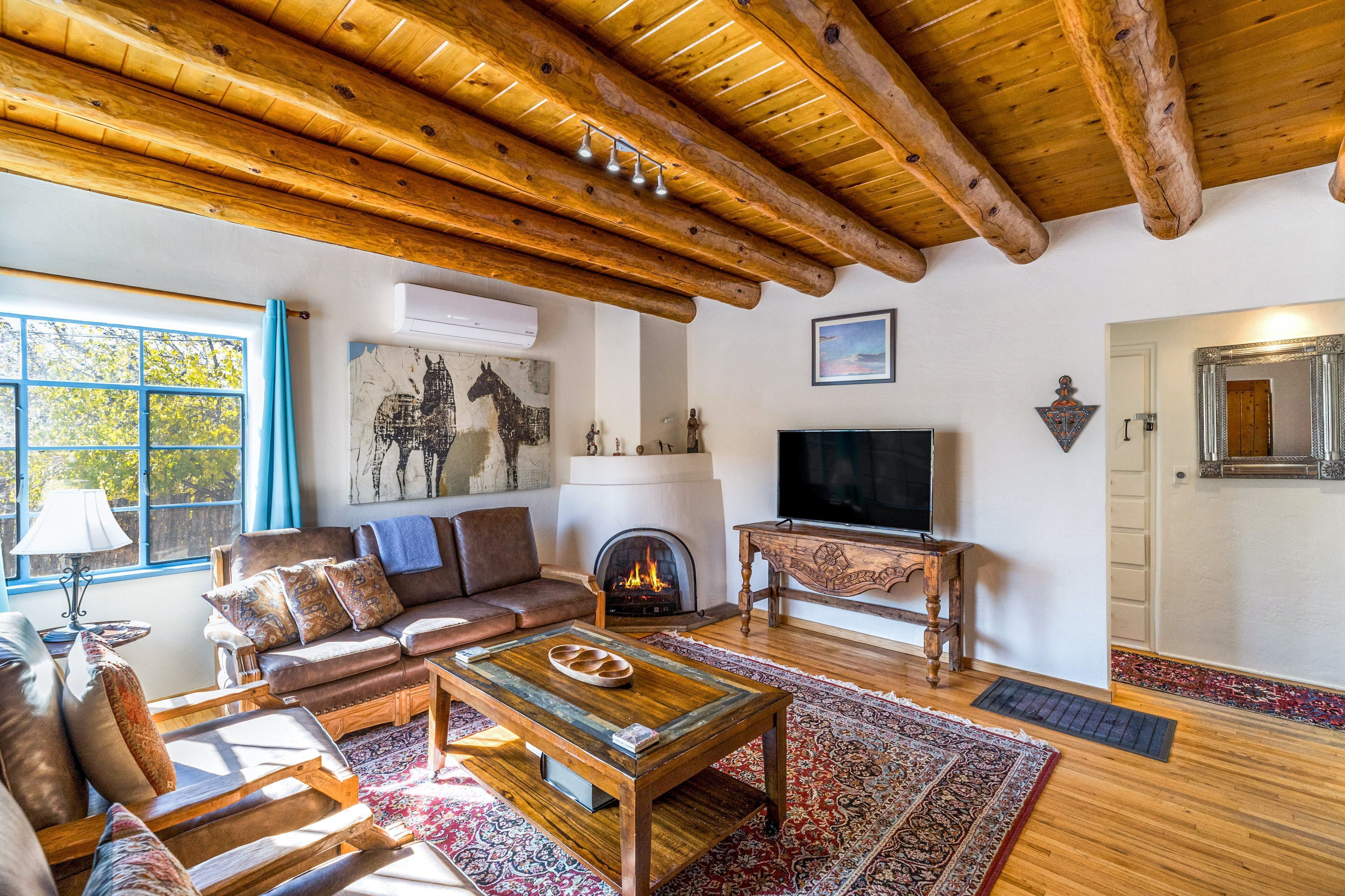 Ein gemütliches Wohnzimmer mit Kamin, Holzbalkendecke, Fernseher und einem großen Fenster mit Vorhängen.