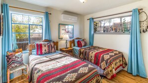A room with two beds, a window with curtains, a wall-mounted air conditioner, and a dreamcatcher decoration.
