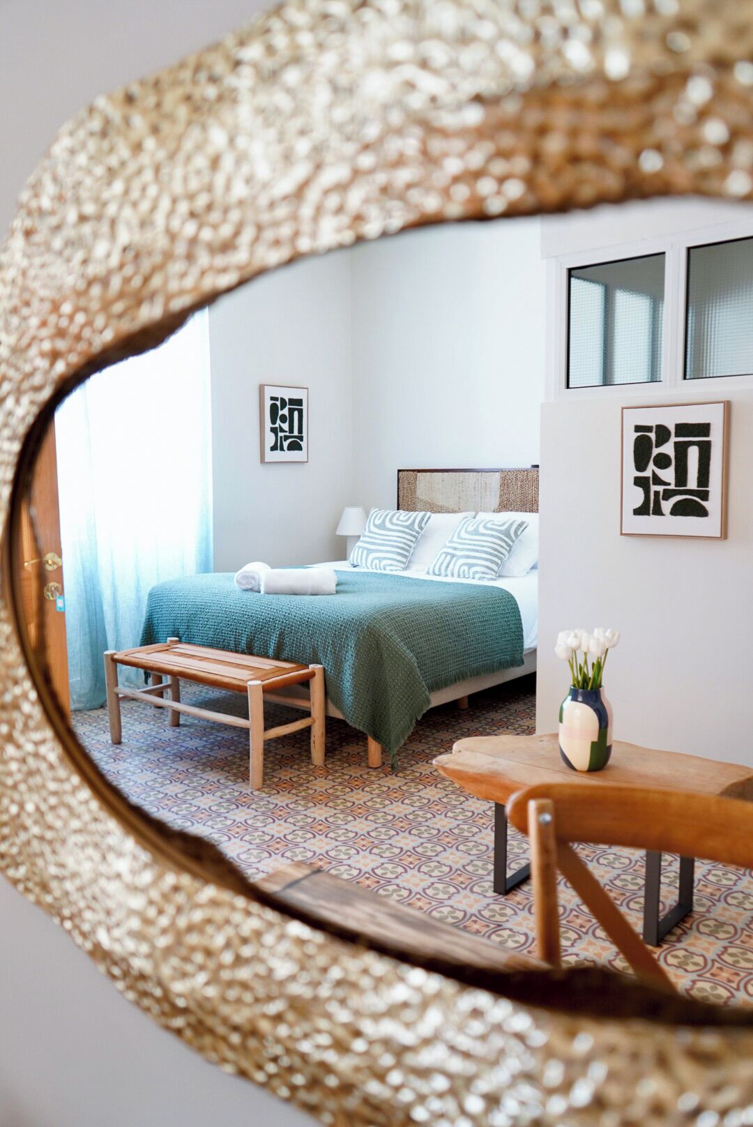 Un dormitorio con una cama, una mesita de noche, una silla, un espejo y una pared decorada con cuadros.