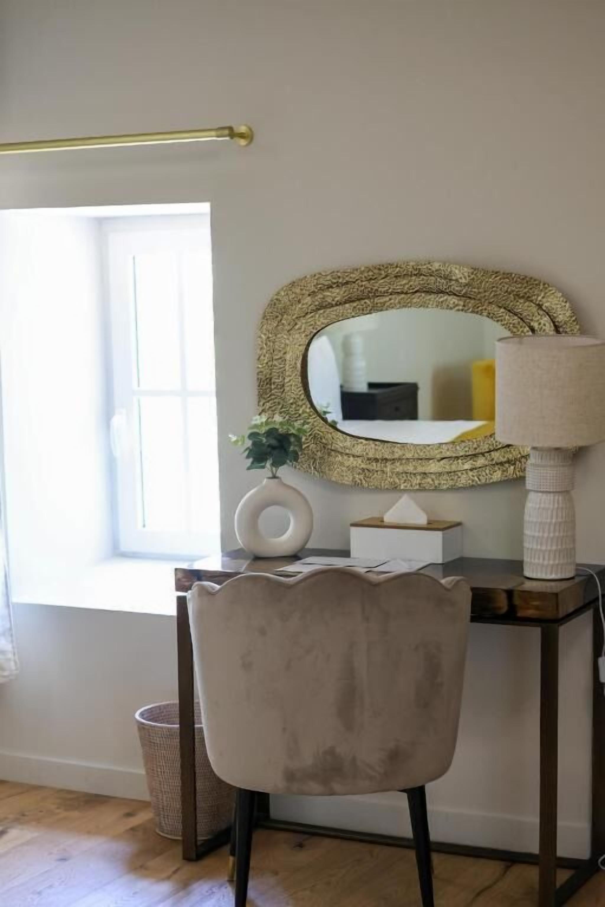 A room with a desk, a chair, a mirror, a lamp, and a window.