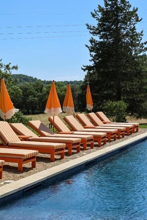 Zona de piscina con sillones reclinables y sombrillas anaranjadas.