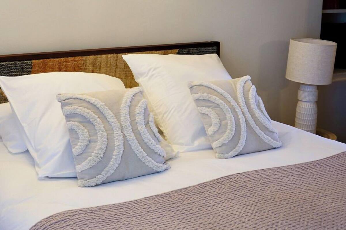 A neatly made bed with a headboard, a bedside lamp, and a wall-mounted air conditioner.