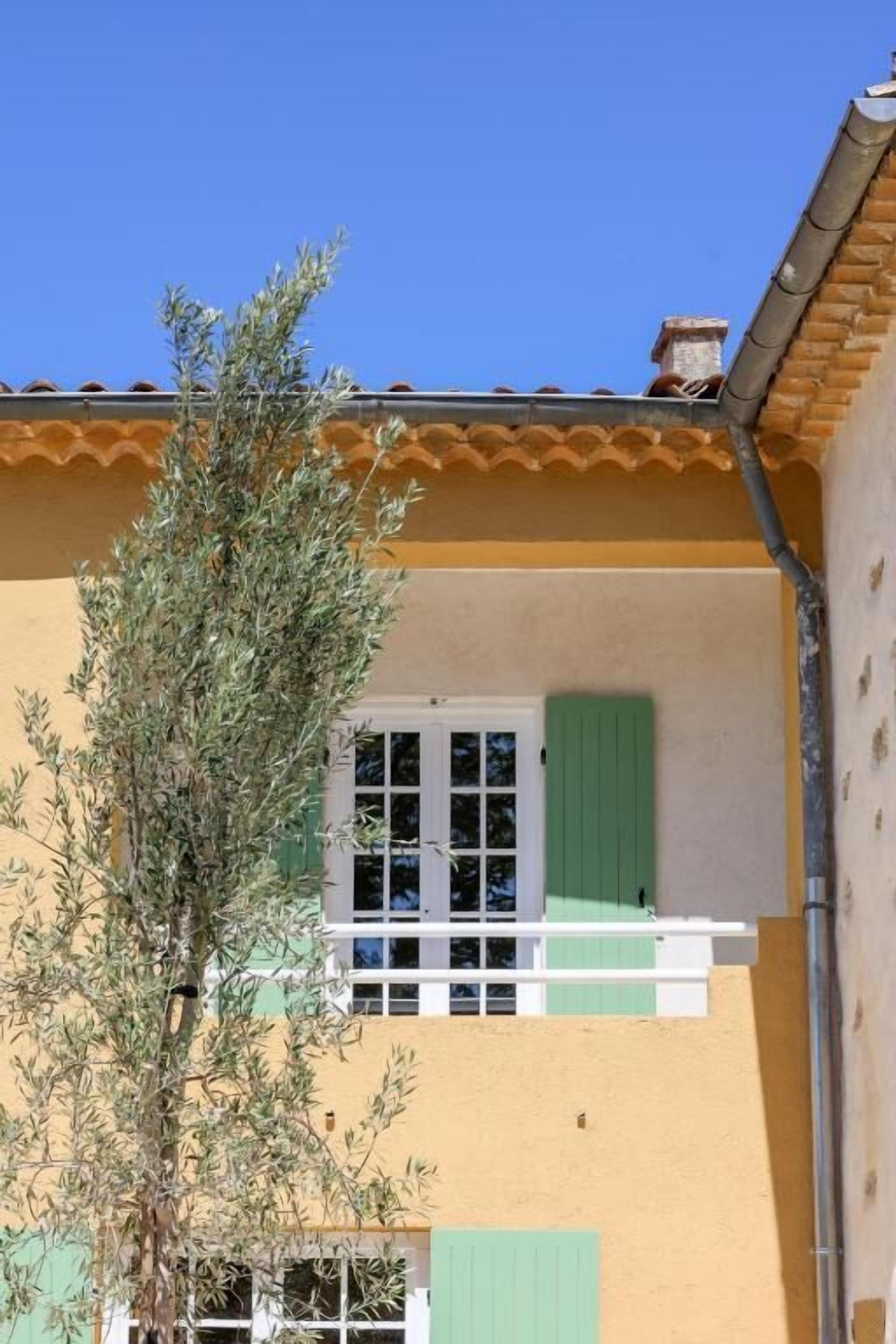 A two-story building with a yellow facade, green shutters, and a visible balcony.