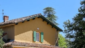 A yellow building with a tiled roof and green shutters, featuring arched windows and a small garden area. - Domaine Robert (Rognes)