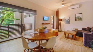 Una sala de estar moderna con una mesa de comedor de madera, sillas blancas, un sofá y un televisor.