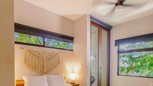 Un dormitorio con cama de madera, ventilador de techo, ventana grande con vistas y un tapiz de macramé.