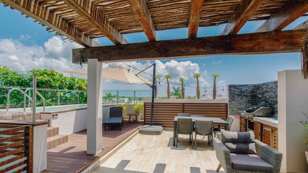 Un patio exterior cubierto con piscina, zona de estar y vistas a palmeras y montañas.