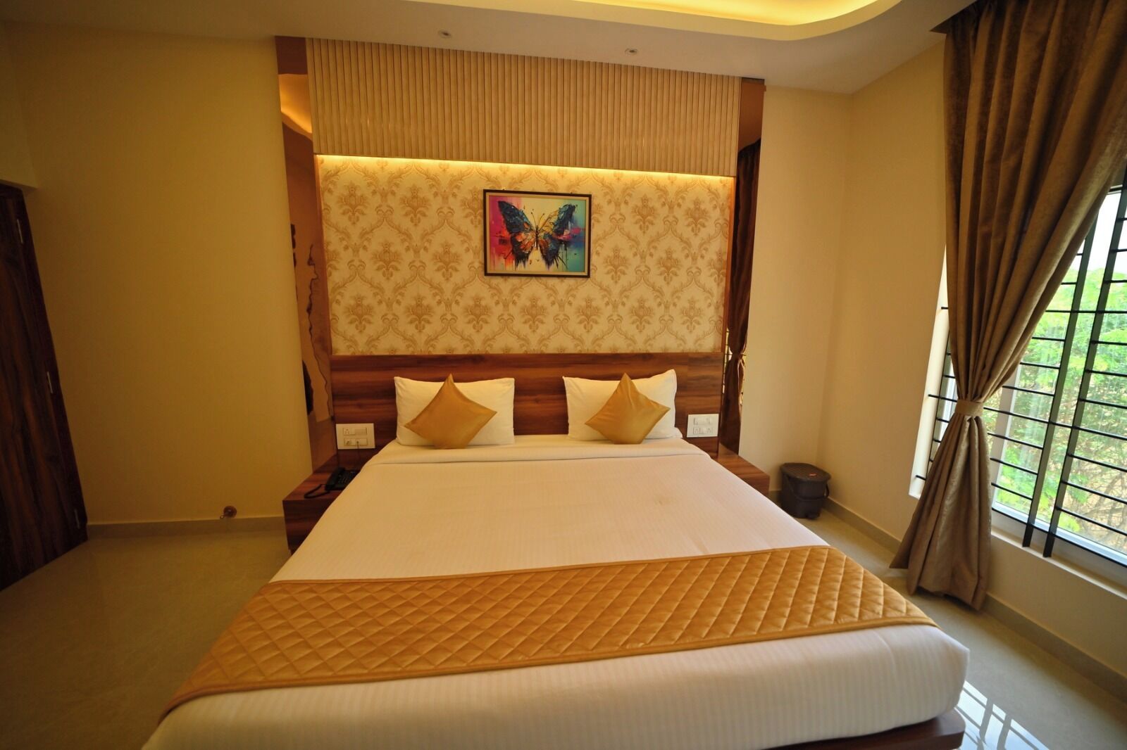 A hotel room with a large bed, a headboard with a butterfly painting, and a window with curtains.