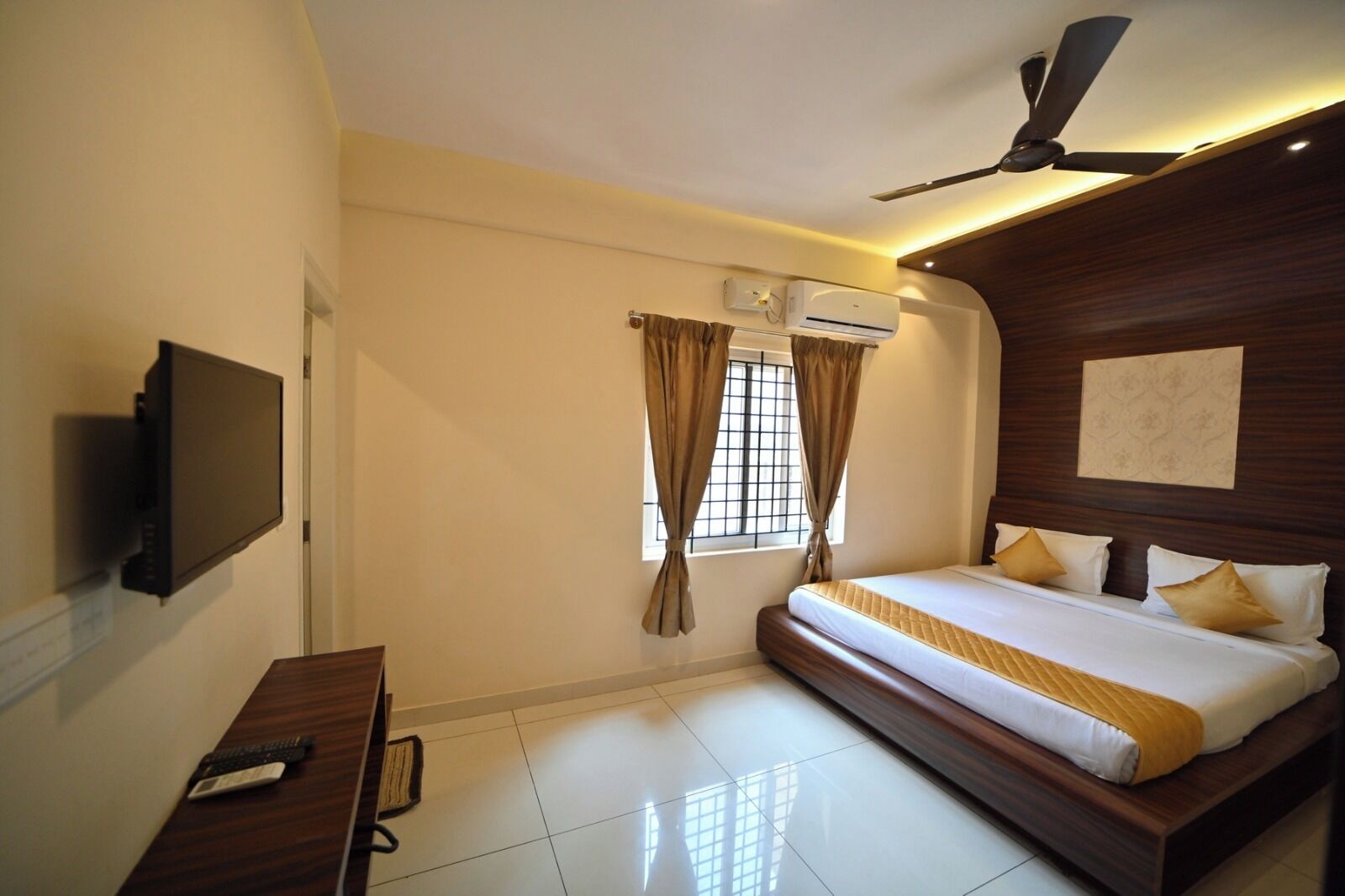 Ein Hotelzimmer mit Bett, Schreibtisch, Fernseher, Klimaanlage und Deckenventilator.