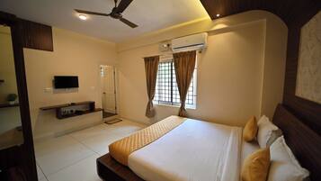 A bedroom with a bed, a ceiling fan, an air conditioning unit, a TV, and a window with curtains.