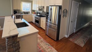 A modern kitchen with white cabinets, stainless steel appliances, a stone accent wall, and a large window. - NEW KI Creek Retreat! 3BR/2bath water view, private house near KI wedding venues (Stevensville)