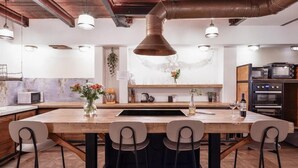 Una cocina moderna con una isla central, taburetes de bar, luces colgantes y un techo rústico.