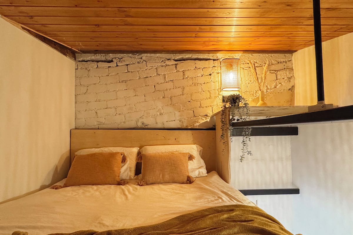 Un dormitorio con techo de madera, pared de ladrillo y cama con dos almohadas.