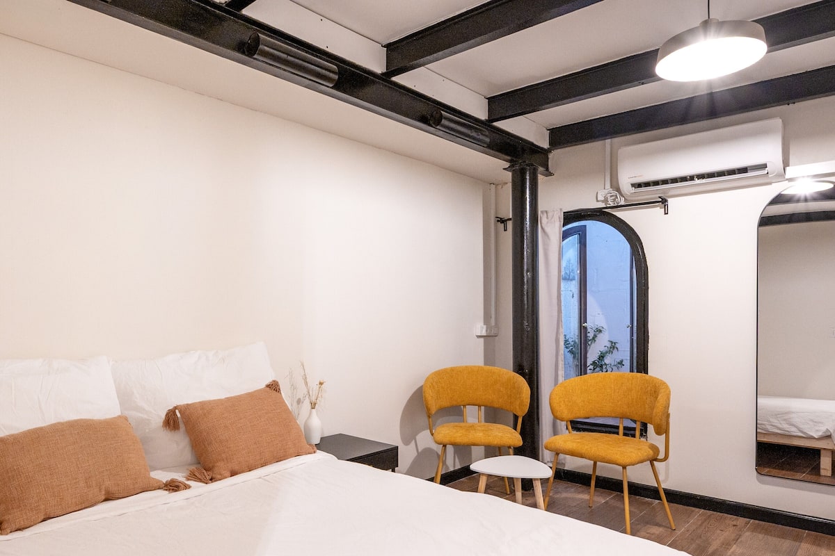 Un dormitorio moderno con una cama grande, dos sillas amarillas, una mesita y un espejo.