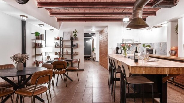 Una cocina moderna con una isla de madera, estantes empotrados y una zona de comedor con sillas y una mesa.