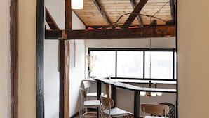 Un interior rústico con vigas de madera a la vista, un techo alto y una zona de comedor con sillas y una mesa.