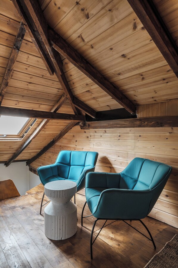 A cozy attic room with wooden beams, a skylight, and two teal chairs with a round table. - The urban chalet (Tel Aviv)