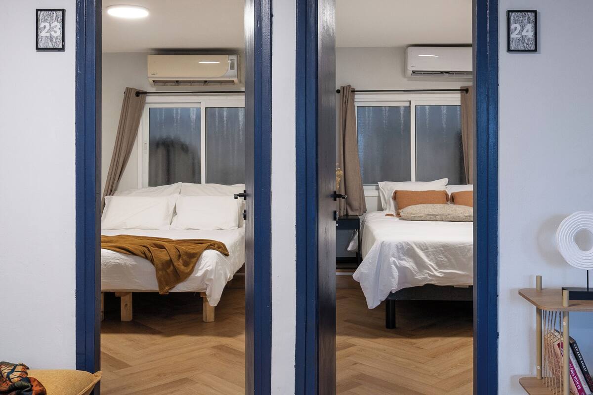 Una habitación de hotel con dos camas, suelo de madera y una mesita con una silla.