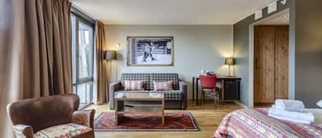 A hotel room with a bed, a sofa, a chair, a small table, and a window with curtains.