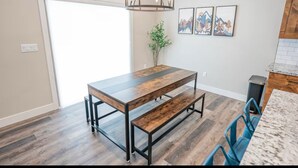A dining area with a wooden table and benches, a hanging light fixture, and framed artwork on the wall. - Ashton Escape - Newly built townhome near Yellowstone/Grand Tetons/Island Park (Ashton)