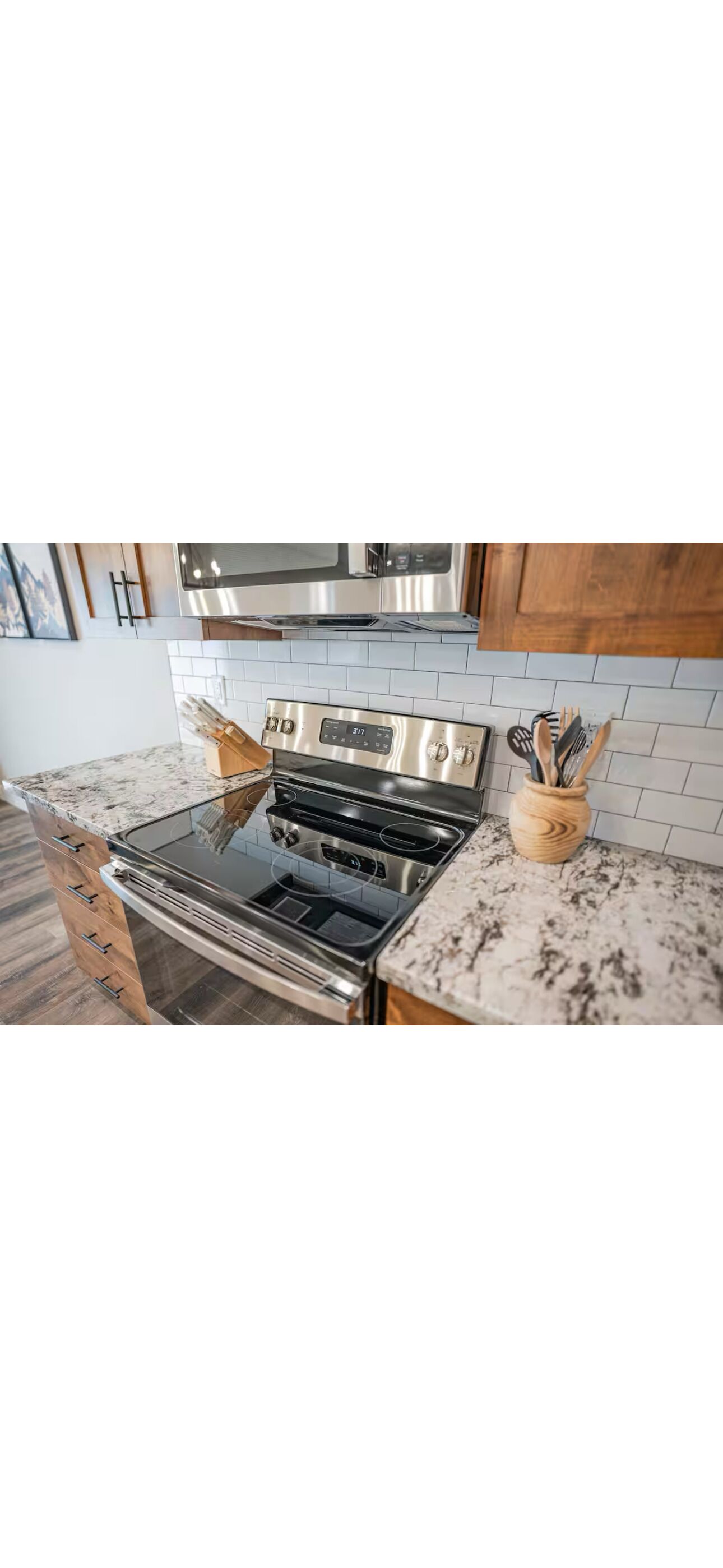 Et køkken med komfur i rustfrit stål, mikroovn og træskabe.