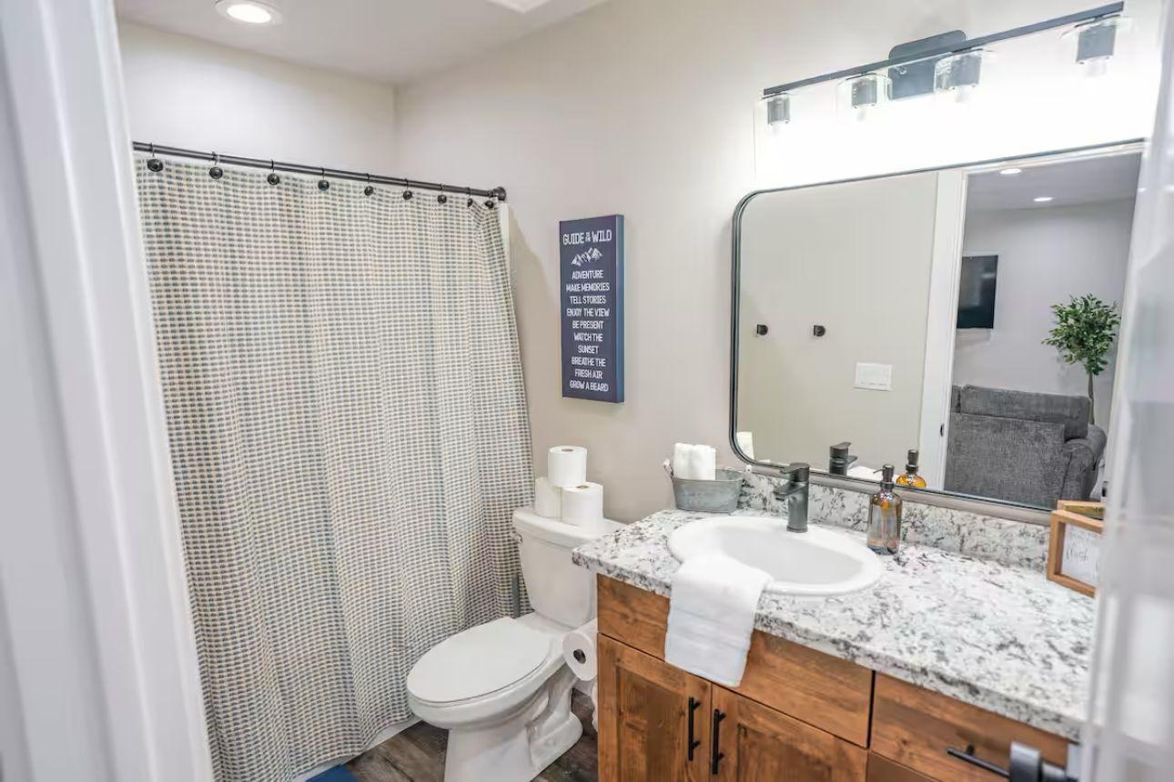 A bathroom with a shower curtain, toilet, sink, and mirror.