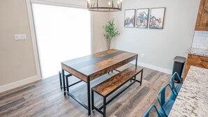 A dining area with a wooden table and benches, a hanging light fixture, and framed artwork on the wall. - Ashton Escape - Newly built townhome near Yellowstone/Grand Tetons/Island Park (Ashton)