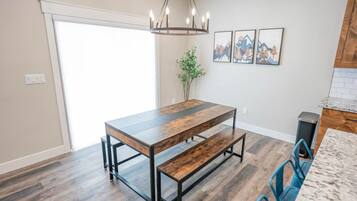 A dining area with a wooden table and benches, a hanging light fixture, and framed artwork on the wall.