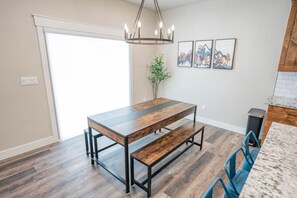 Ein Essbereich mit Holztisch, Bänken, einer Pendelleuchte und gerahmten Bildern an der Wand.
