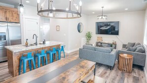 A modern kitchen with a central island, blue bar stools, and a chandelier. - Ashton Escape - Newly built townhome near Yellowstone/Grand Tetons/Island Park (Ashton)