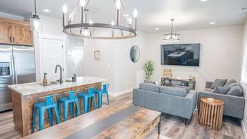 A modern kitchen with a central island, blue bar stools, and a chandelier.