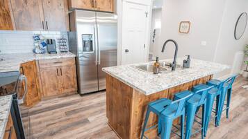 A kitchen with wooden cabinets, a stainless steel refrigerator, a marble countertop, and blue bar stools.