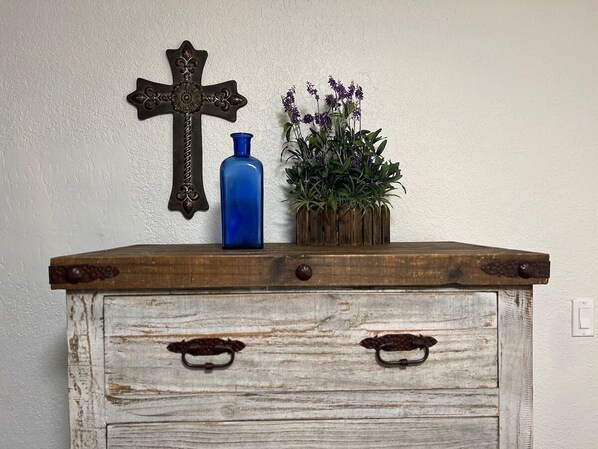 A rustic wooden dresser with two drawers and a cross on the wall above it.
